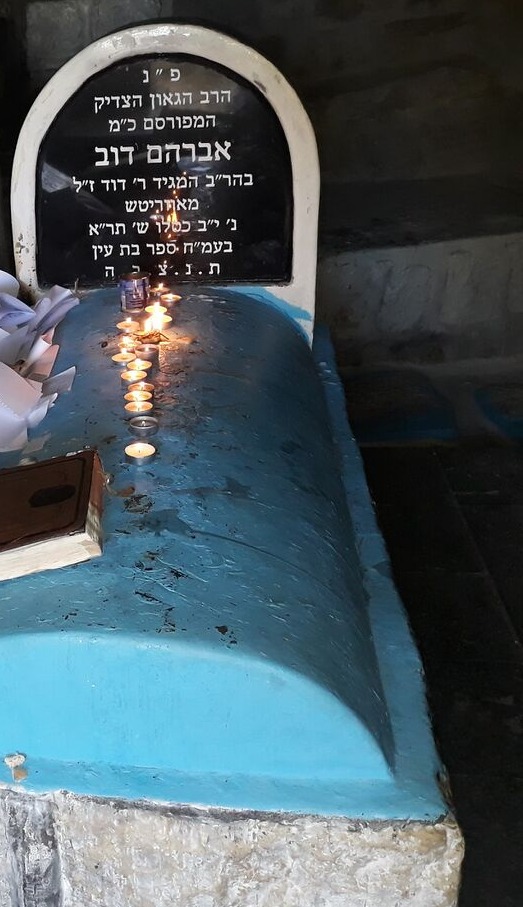 The matzeivah and blue kever of the Bas Ayin in Tzfas's ancient cemetery, with candles and kvitlach on the kever